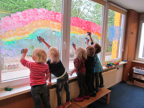 Kinder malen am Fenster einen Regenbogen